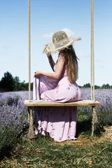 Foto op Aluminium Young sexy beautiful woman enjoying the rays of the sun while sitting on a hanging vintage swing in a lavender field against the sky.  © fotodiya83