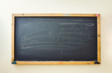 Old blackboard with wooden frame hangs on wall in classroom. Board surface with white chalk marks after challenging lesson at school.