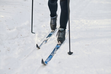 Legs of unrecognizable man in sportswear skiing along road covered with snow on cold winter day, copy space