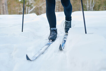 Legs of unrecognizable sportsman skiing along trail covered with snow on winter day, copy space