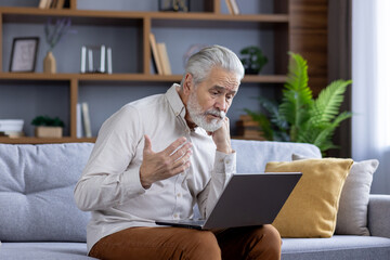 Upset senior gray-haired man talking on video call with family and bank, sitting on sofa and...