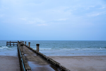 One fishing man on the old long concrete pier extending out into the ocean with cloudy in the sky background in Chumphon Province, Thailand.