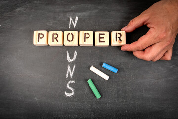 Proper Nouns. Wooden block crossword puzzle and pieces of chalk on a chalkboard background - 794351973