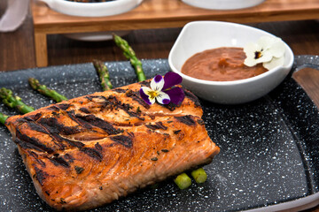 Grilled salmon garnished with asparagus, sauces and dressings on restaurant table, decorated with flowers