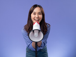 asian woman with megaphone, blue blouse, making an announcement on a vibrant purple background