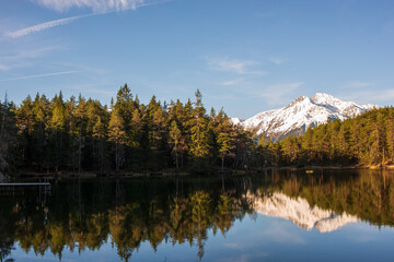 Snow-capped mountain reflected in the still waters of a forest-fringed lake under a clear blue sky.