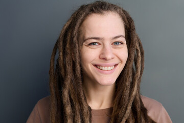 Minimal close-up portrait of smiling young woman with long dreadlocks looking at camera on grey