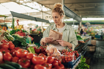 Female customer with paper bag choosing fresh vegetables.