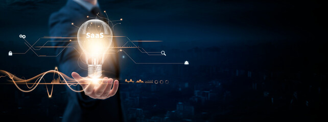 SaaS: Businessman holding creative light bulb with Digital networking and SaaS icon. Cloud Solutions, Subscription-Based Software, Innovation, Empowering Businesses, on blue city background.