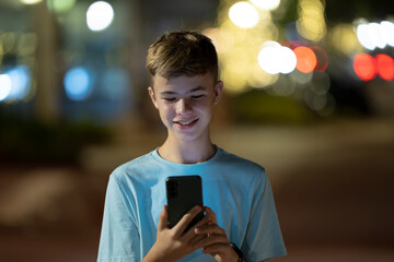 Happy teenager boy playing video games on his cellphone on night street.