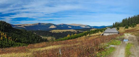 An old sheepfold rests amidst rolling hills and lush forests under a blue sky, showcasing the natural beauty of the mountains. The scene reflects serene outdoor living. Autumn season in Carpathia