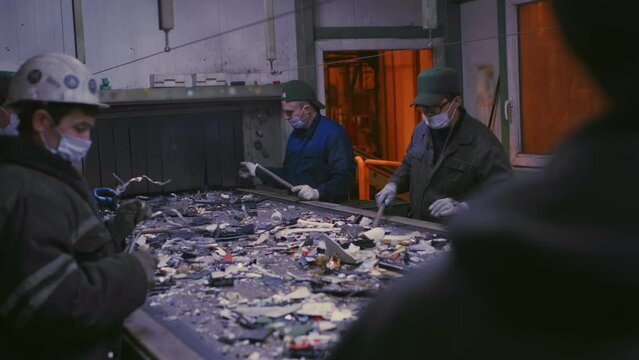 Trash sorting. Conveyor for waste. Recycling garbage. Men sort metal garbage on a conveyor. Recycle process, secondary use of plastic. Recycling factory. Male workers recycle scrap metal. Littering