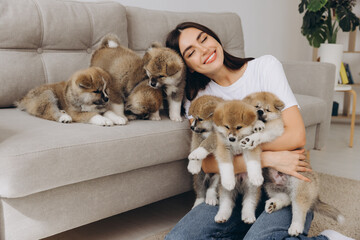 Portrait of happy smiling millennial woman, new owner, hugging group Akita Inu puppies on sofa at...