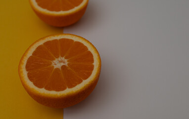 oranges are cut in half and placed on a yellow and white background. The oranges are ripe and juicy, and their bright orange color contrasts with the neutral background
