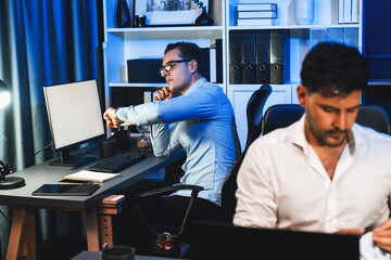 Colleagues concentrating on their job task at night home office behind desk while another man with thoughtful face solving to postpone the deadline of project at the blurred front side. Sellable.