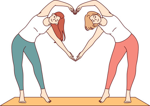 Paired yoga of two women doing aerobics or pilates standing on sports mat and making heart sign from hands. Attractive girls are interested in fitness and pilates to avoid excess weight