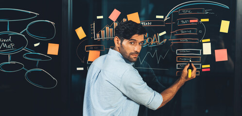 Portrait of skilled businessman writing marketing idea on glass wall with chart, mind map and...