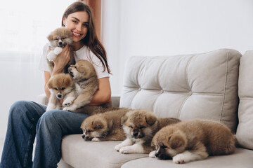 Portrait of happy smiling millennial woman hugging and playing group Akita Inu puppies on sofa at home