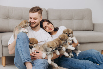 Beautiful smiling happy couple playing with akita inu puppies in dog house or shelter