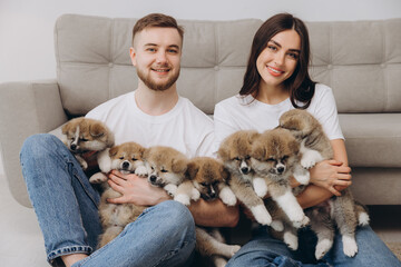 Beautiful smiling happy couple playing with akita inu puppies in dog house or shelter