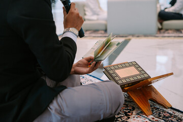 Image depicts a person immersed in reading the Quran inside a mosque, reflecting devotion and...