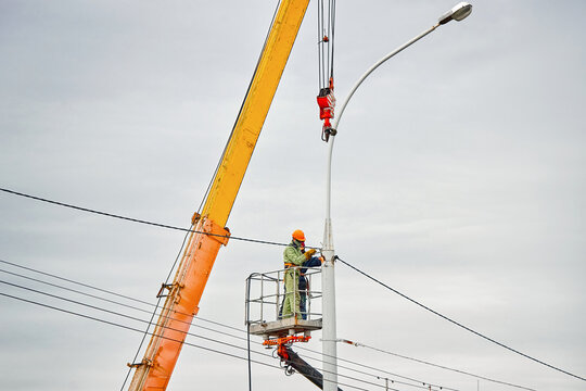 Construction workers in cherry picker welding street light pole. Street light repair works, workers team repair street lamp at height, teamwork. Men in lift bucket weld street pole.