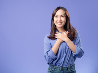 Cheerful Asian woman holding a laptop and a credit card, ready for online shopping, against a purple background