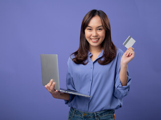 Cheerful Asian woman holding a laptop and a credit card, ready for online shopping, against a...