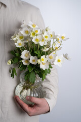 Man holding white anemone in his hands. Beautiful spring flowers. The florist man gathered a...