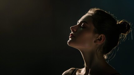 A profile portrait of a ballet dancer in a dark studio with their face softly illuminated by a spotlight capturing the delicate beauty and vulnerability of their art form. .
