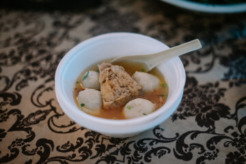 A bowl of meatball soup with a piece of tofu on a stereotypical bowl, capturing the essence of Indonesian street food culture