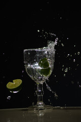 Splashes coming out of a glass cup with clear water caused by a slice of lemon. Isolated on dark background.