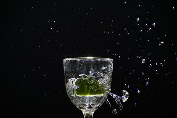 Splashes coming out of a glass cup with clear water caused by a slice of lemon. Isolated on dark background.