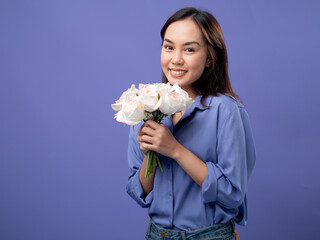 Radiant woman holding a bouquet of roses, blue shirt and jeans, symbolizing joy on a purple background