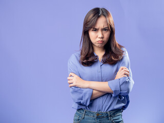 Displeased Asian woman in a casual blue blouse standing with arms crossed, expressing...