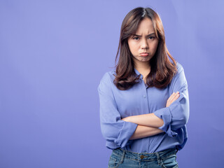 Displeased Asian woman in a casual blue blouse standing with arms crossed, expressing...