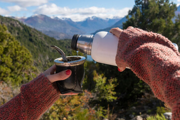 Hands holding a mate with Argentine yerba, with mountains and lakes in the background. Patagonia, Argentina. - obrazy, fototapety, plakaty
