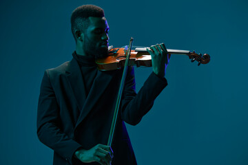 Elegant African American man playing the violin in a stylish black suit on a vibrant blue background
