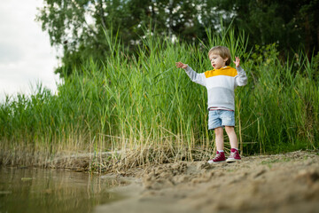 Cute little boy playing by a lake or river on hot summer day. Adorable child having fun outdoors during summer vacations.