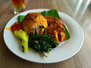 A plate of complete Nasi Rendang meal served with sweet iced tea, showcasing a flavorful Indonesian culinary experience in one serving