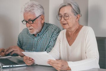 Elderly senior family couple reading paper correspondence or mails, sitting at home with computer....