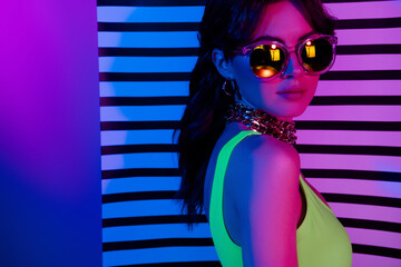 Photo of cool girl in sunglass stand profile side look camera over striped wall neon ultraviolet...