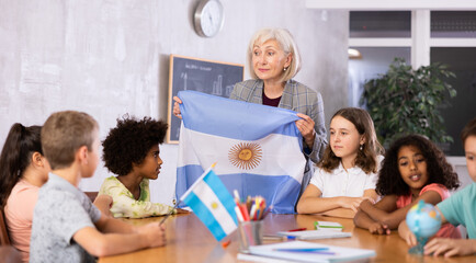 Mature woman teacher working in a high school tells pupils the history of Argentina in class and...