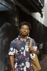 young black man standing outside with bag looking at the camera