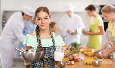 Curious teen girl participating in culinary workshop led by professional chefs for tweens and learning how to cook..