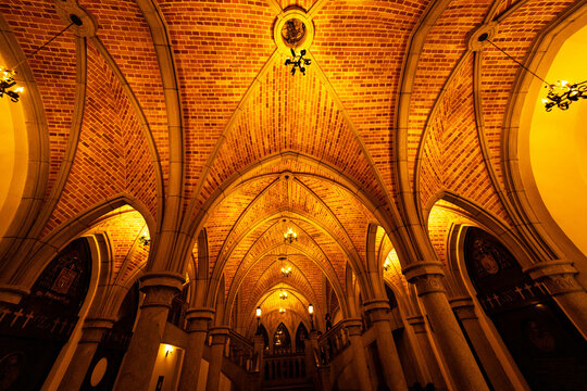 Cripta com teto alto, coluna, arco e lustre de luz amarela. 