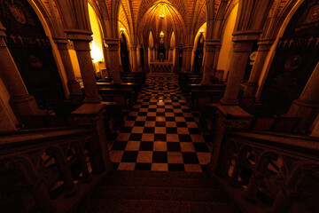 Salão de cripta, arcos, portas, lustre, e piso xadrez. 