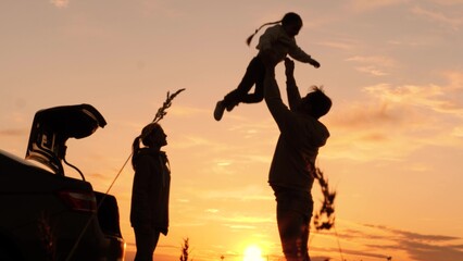Silhouette of father tossing child in air. Family traveling by car having fun in nature laughing...