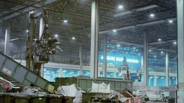 A mechanical crane at a waste recycling plant. Recycling of plastic, metal and microchips. Clamshell scoop closes around materials securing tightly for transporting to processing area