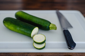 Two Zucchini, one sliced, one whole on a white cutting board with chefs knife